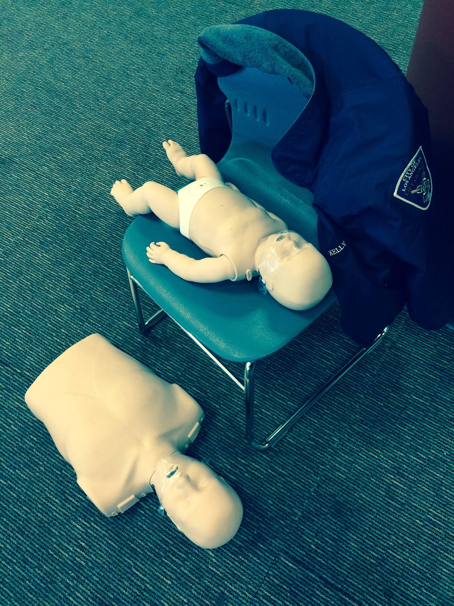 Infant CPR manikin and adult CPR training torso beside an LA County Lifeguard jacket